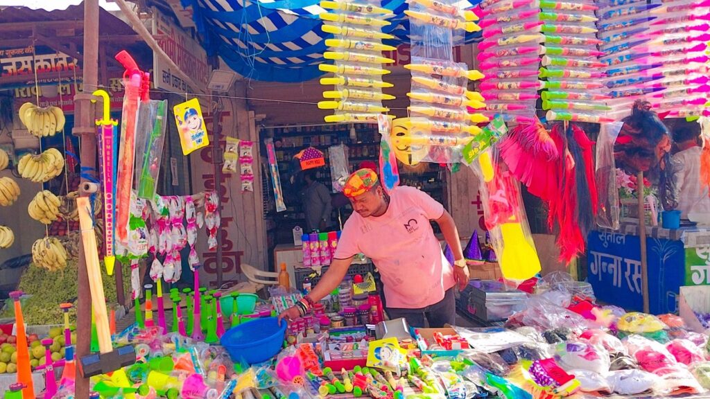 होली रंगों की त्यौहार” रंग बिरंगी पिचकारी और होली सामग्री से सजी बाजार।